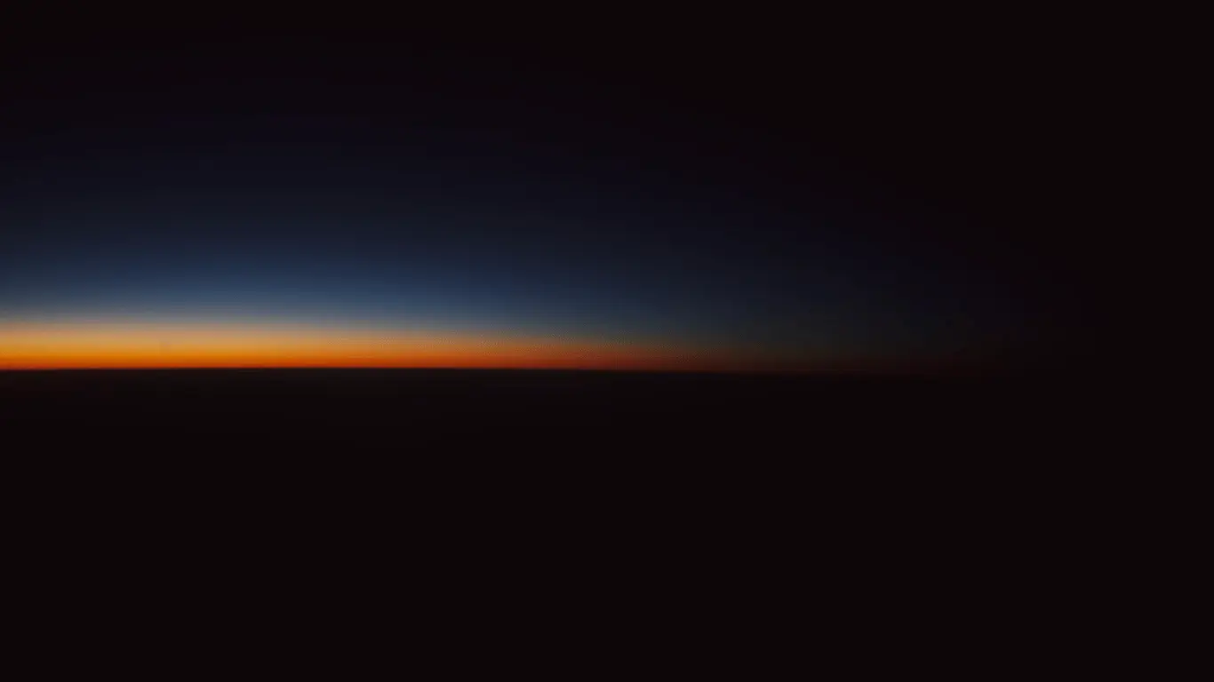 The gradient of dawn over a completely unobstructed sea horizon, from night blue to orange, without a single feature in the way.