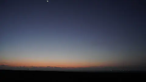 Un fin croissant de Lune et le point brillant de Vénus dans les dernières couleurs du crépuscule.