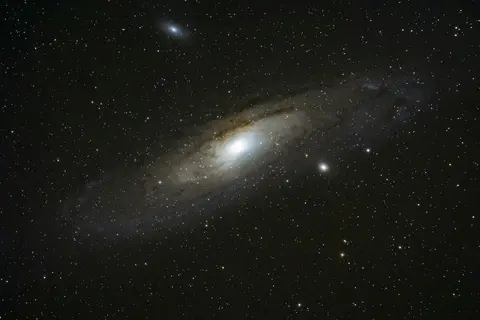 La galaxie d'Andromède, M31, photographiée au téléobjectif : le disque incliné, le noyau brillant et ses deux galaxies compagnes.