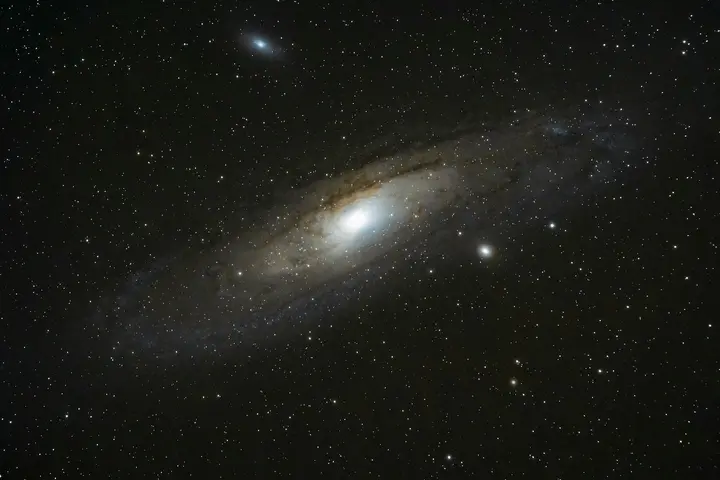 La galaxie d'Andromède, M31, photographiée au téléobjectif : le disque incliné, le noyau brillant et ses deux galaxies compagnes.